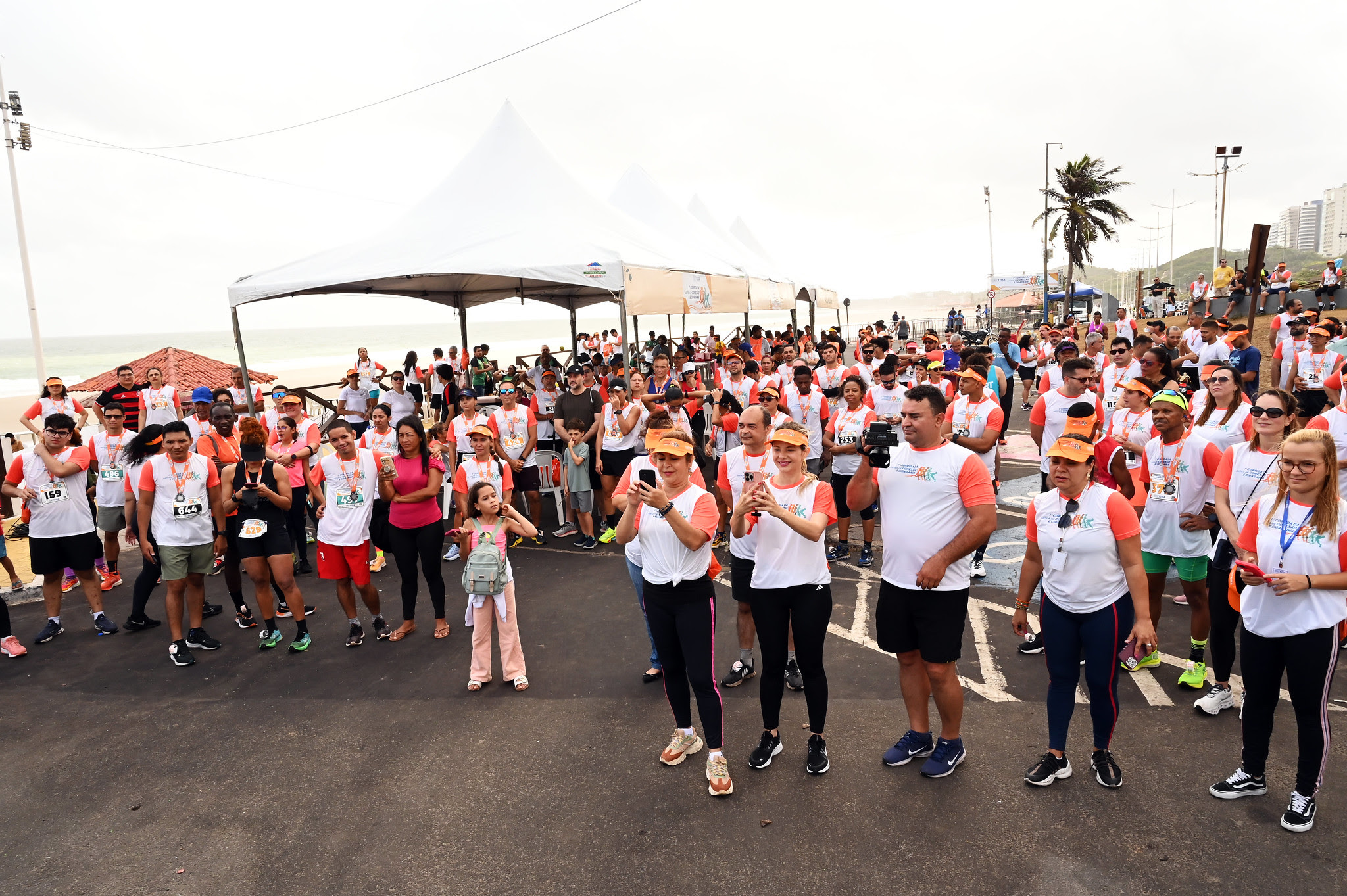 A imagem mostra um grupo de indivíduos em um palco, dentre elas o presidente do TJMA, desembargador Froz Sobrinho, e ganhadores da corrida. . Eles estão vestindo roupas atléticas e números de identificação, sugerindo que participaram de um evento de corrida. Uma pessoa está sentada em uma cadeira de rodas, indicando a inclusão de participantes com diferentes necessidades de mobilidade. Ao fundo, há banners com logotipos, provavelmente representando patrocinadores ou organizadores do evento. Esta imagem captura um momento de conquista e camaradagem entre os diversos participantes de uma competição atlética.