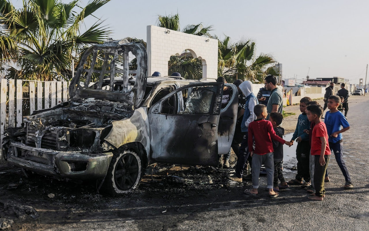 People stand near a destroyed car of the NGO World Central Kitchen (WCK) along Al Rashid road, southern Gaza strip