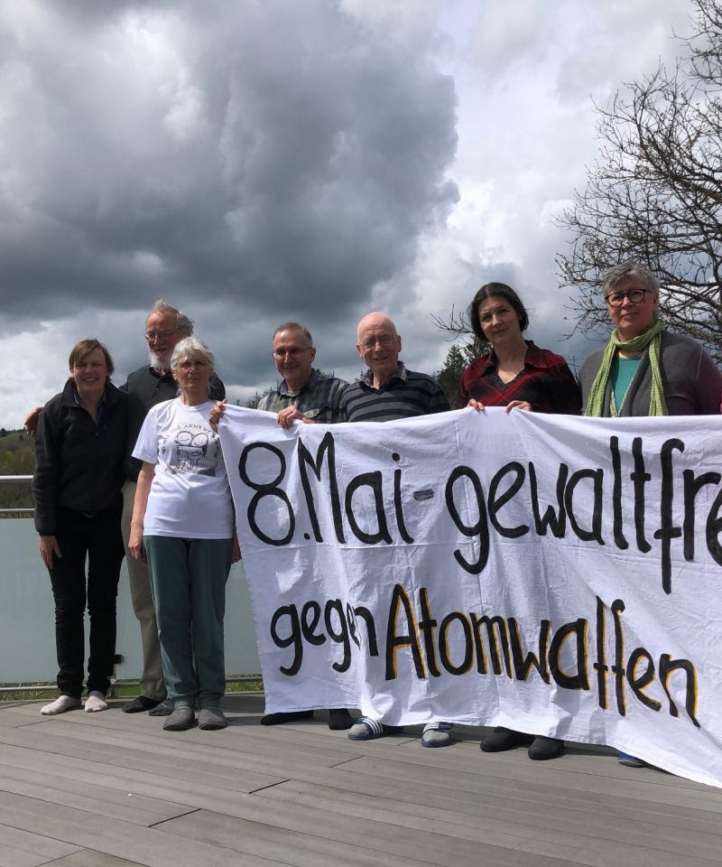 A group of 8 people stand, holding a banner with an anti-nuclear message written on it in German