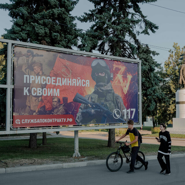 Two young men walking past a billboard showing multiple soldiers.