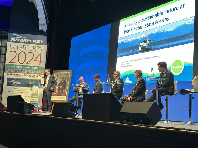 Six people on stage with five seated and one standing presenting on "Building a Sustainable Future at Washington State Ferries"