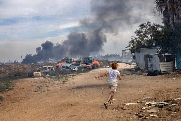 A woman running to hide in a shelter as smoke rises in the distance.