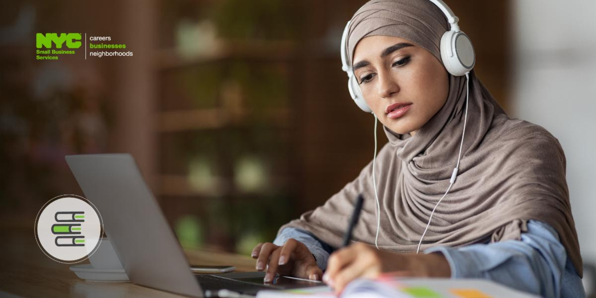 Woman with headphones on writing while sitting in front of a computer