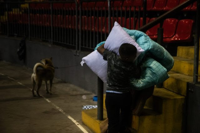 Menino carrega cobertas e colchões para uma parte alta do Ginásio Municipal Celso Morbach