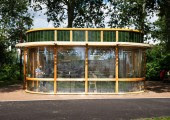 La estructura tiene una fachada curva con un remate de loza verde sobre grandes muros de cristal separados por pequeñas columnas de madera.
