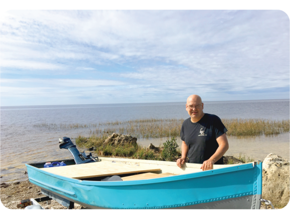 Man standing behind a blue boat on the coast 