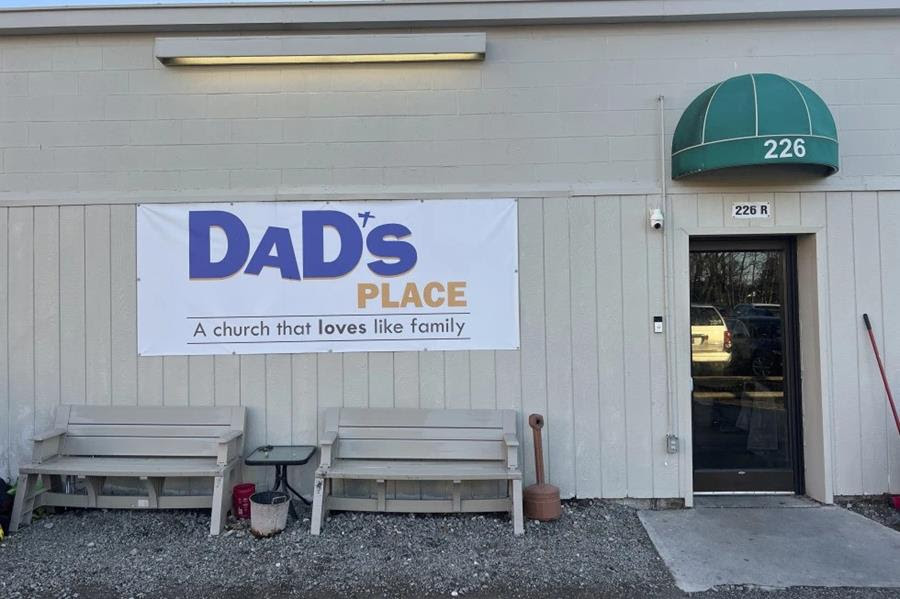 The side of a building with a banner that says "Dad's place: A church that loves like family." There is also a glass door under a green awning that has the numbers 226 on it.