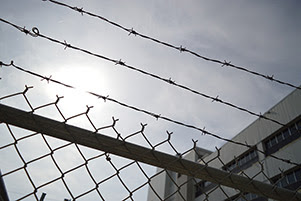 A building is behind a chain link fence with barbed wire security at the top.