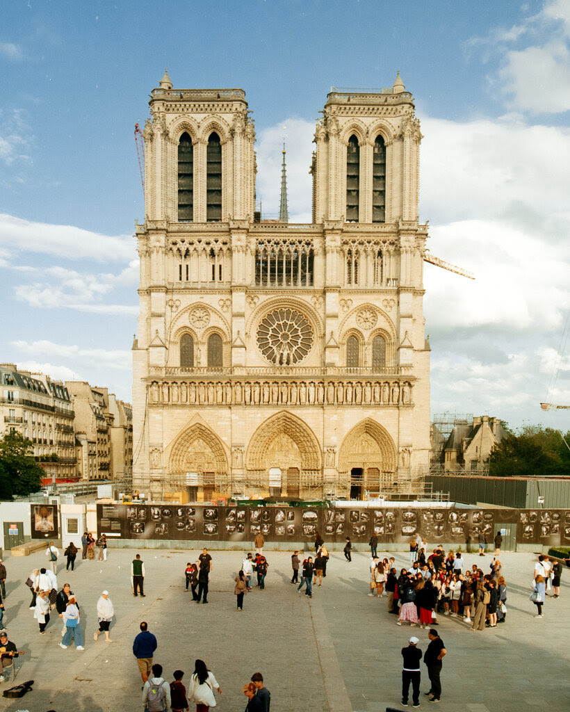 A view of people gathering in front of the Cathedral of Notre-Dame in Paris in June, with construction barricades at ground level.