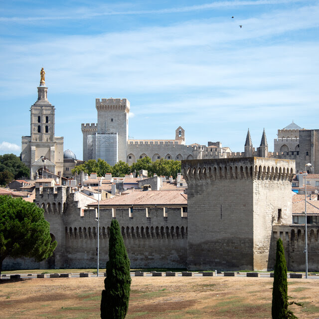 A view of the rooftops of Avignon, showing centuries-old stone towers against a blue sky.