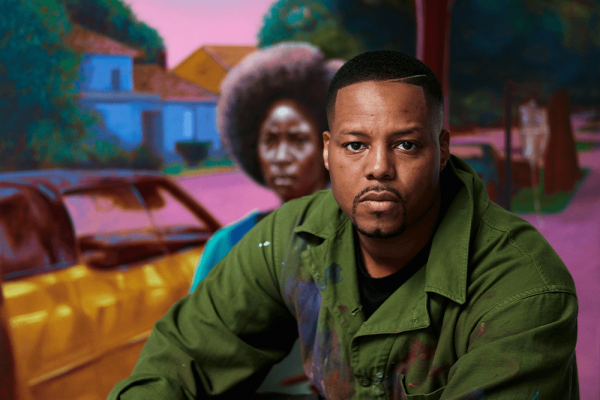 Titus Kaphar (Black man wearing green shirt) poses in front of a still from his film