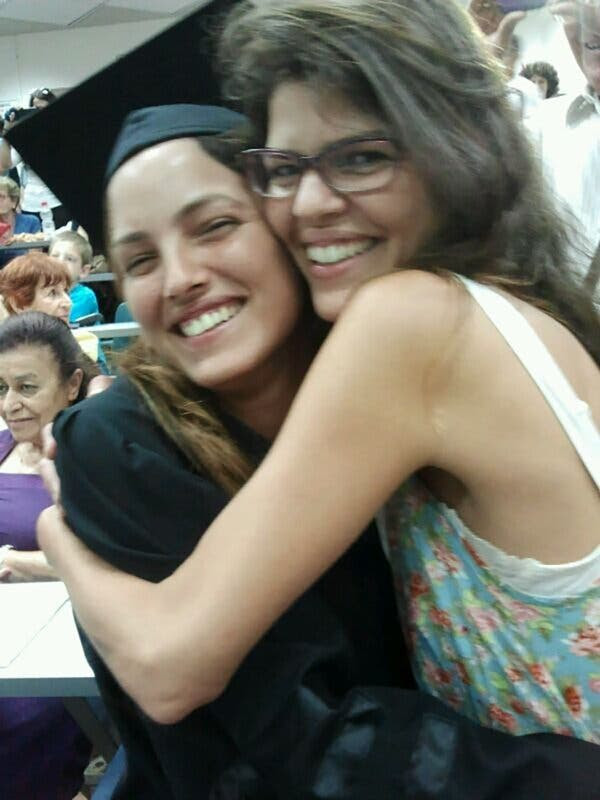 Two women embrace. One is wearing a graduation outfit.