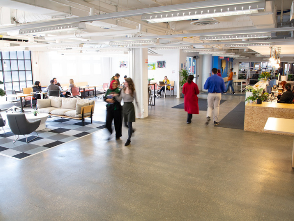 People walking around, sitting at tables and desks, and others sitting behind a front desk in a coworking office space