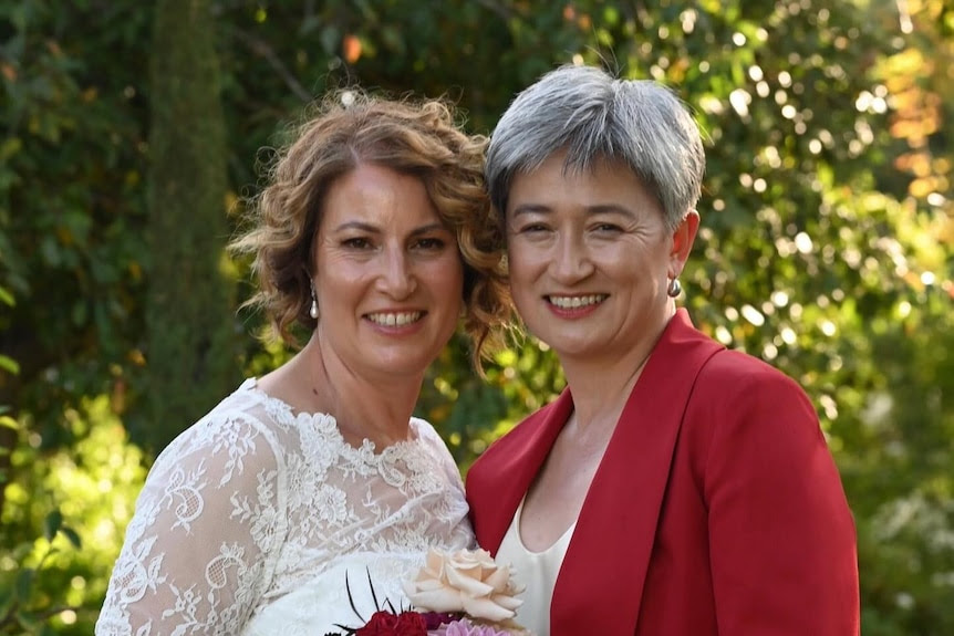 Sophie Allouache in a white dress and Penny Wong in a red blazer stand together smiling.