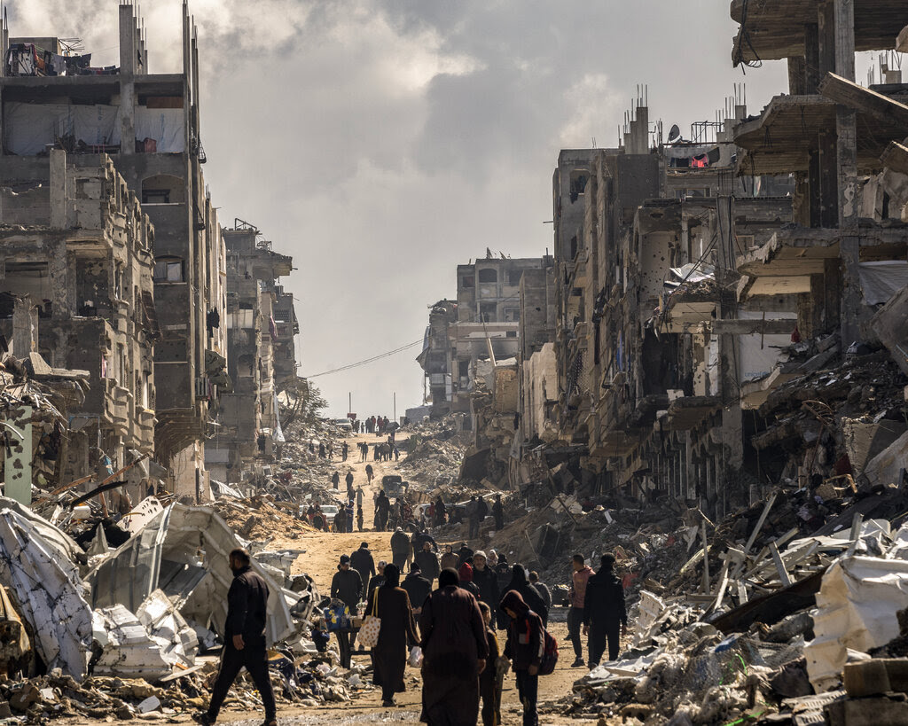 People walk among the rubble of destroyed buildings.