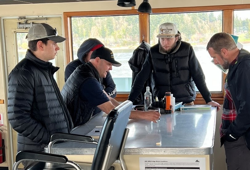 Several people gathered around a table in the pilothouse of a ferry