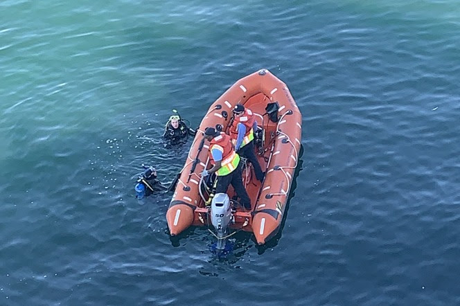 Two ferry crew members in a rescue boat with two divers in the water alongside the vessel