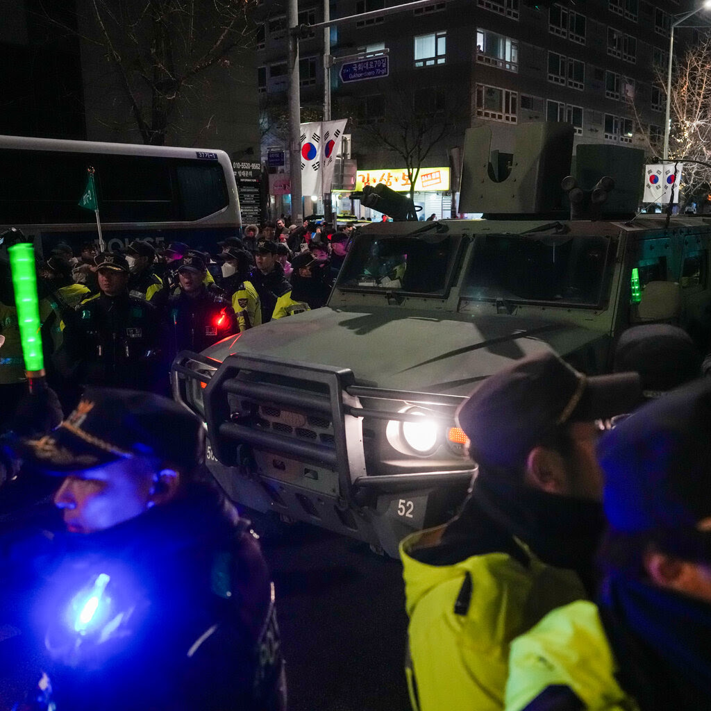 A military vehicle surrounded is surrounded by law enforcement officers and protesters outside the National Assembly in Seoul.