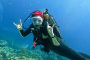 Rebecca Ruiz poses underwater in scuba diving gear giving a "rock on" hand gesture