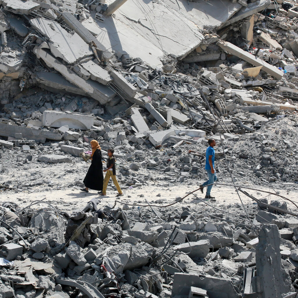 A woman and a young girl walking on a dusty path cutting between enormous mounds of rubble. 