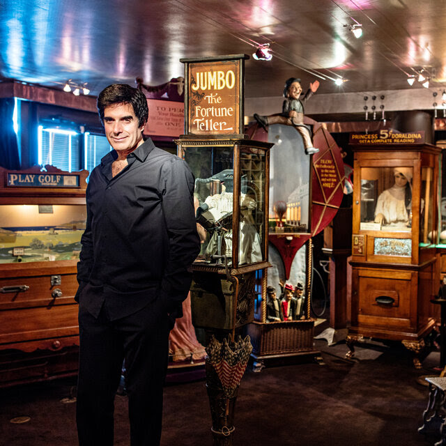 David Copperfield standing in front of a collection of old-time carnival machinery.