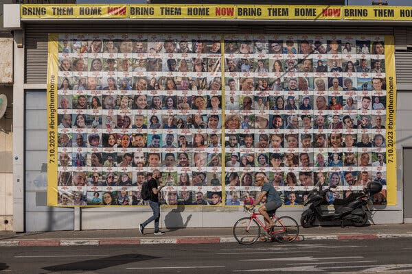 Un gran cartel al aire libre con decenas de fotografías de personas. “Tráelos a casa”, se lee en el texto encima de ellos.