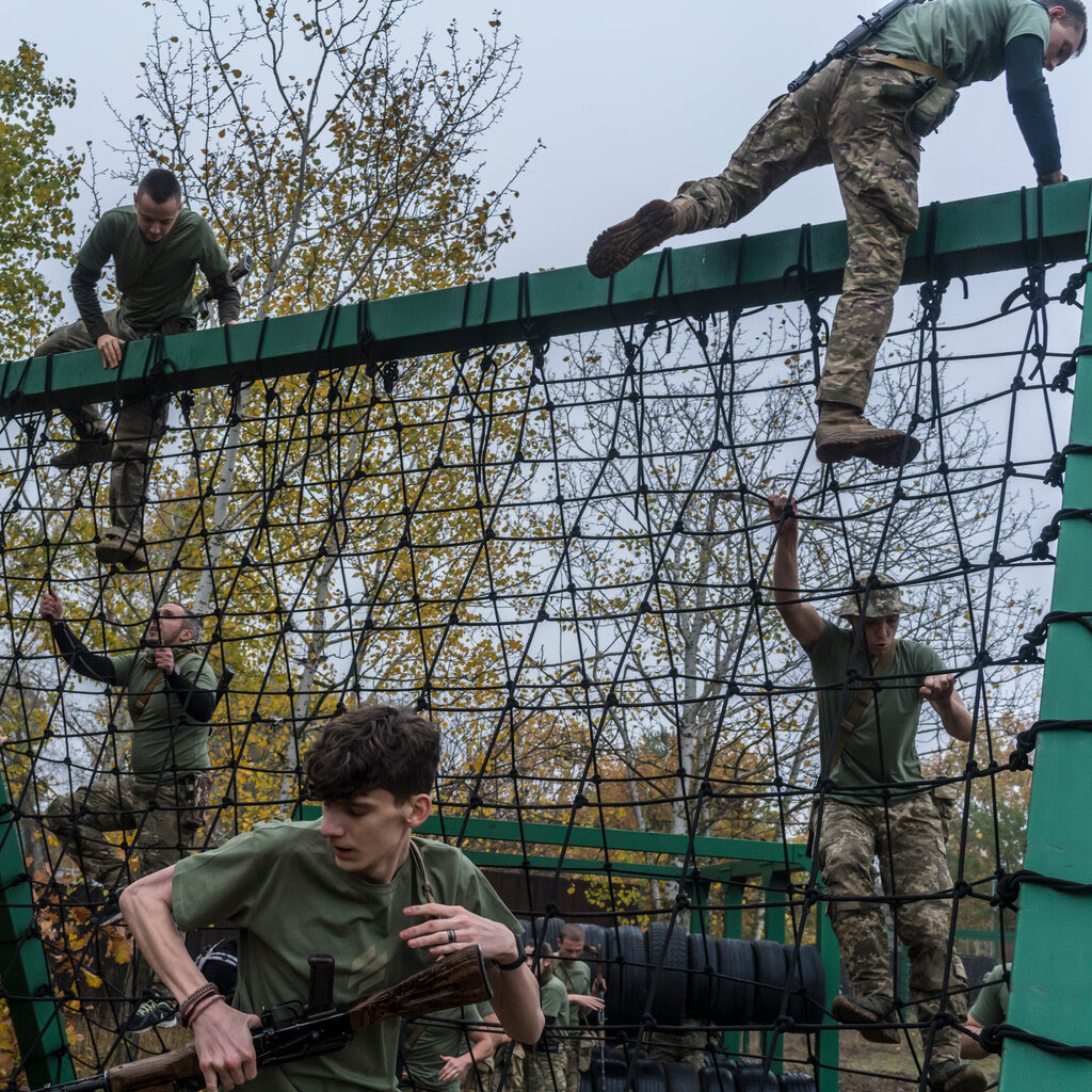 People in military uniform climbing up and over a piece of training equipment.