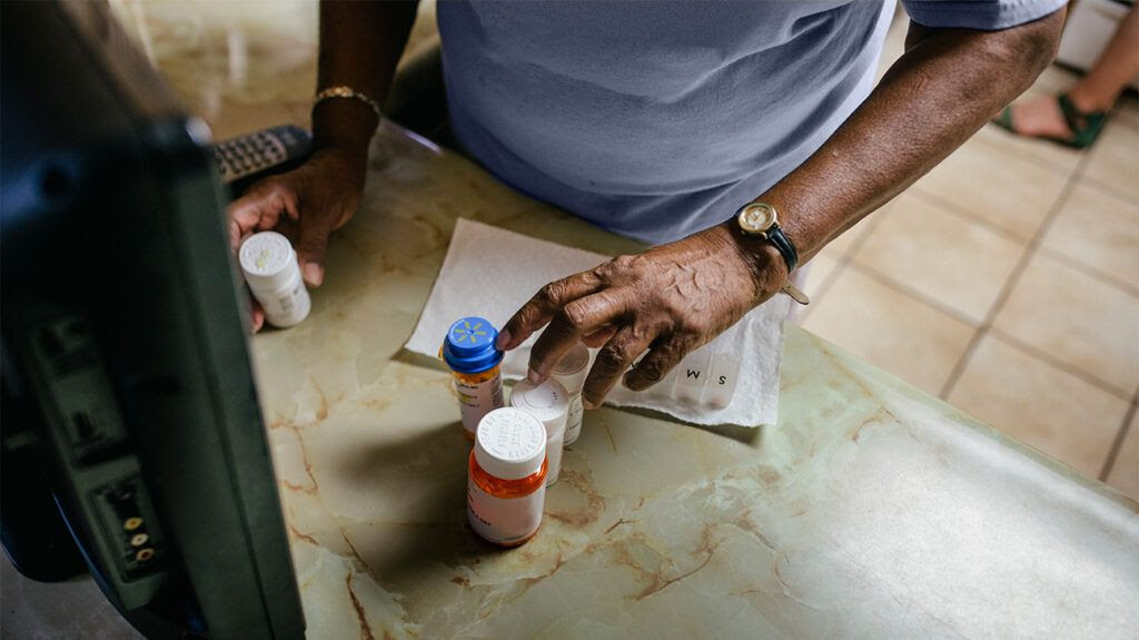 older Black person's hands hovering over pill boxes