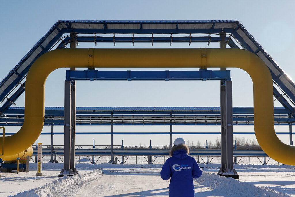 A person stands in front of a pipeline that curves up and over another structure. It is snowy outside.