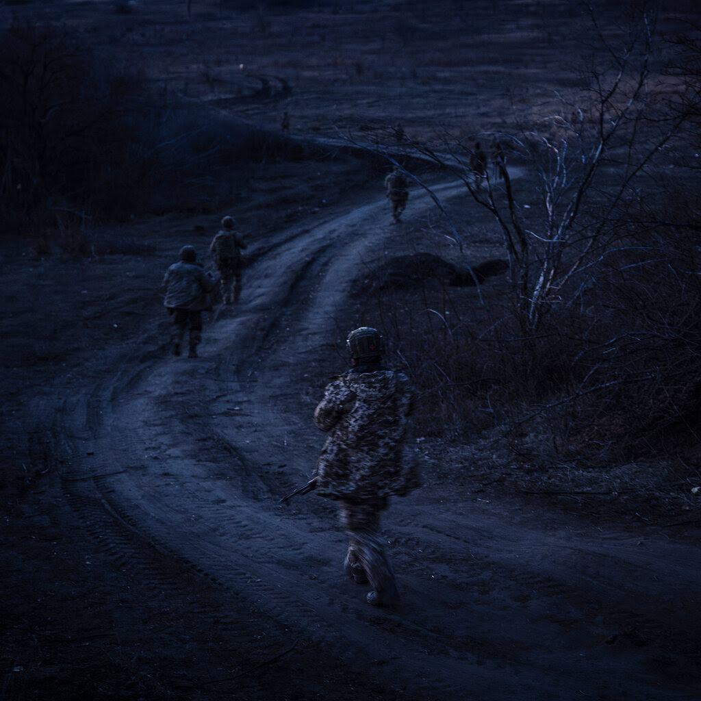 Soldiers walk along a dirt road in the blue light of dusk. 