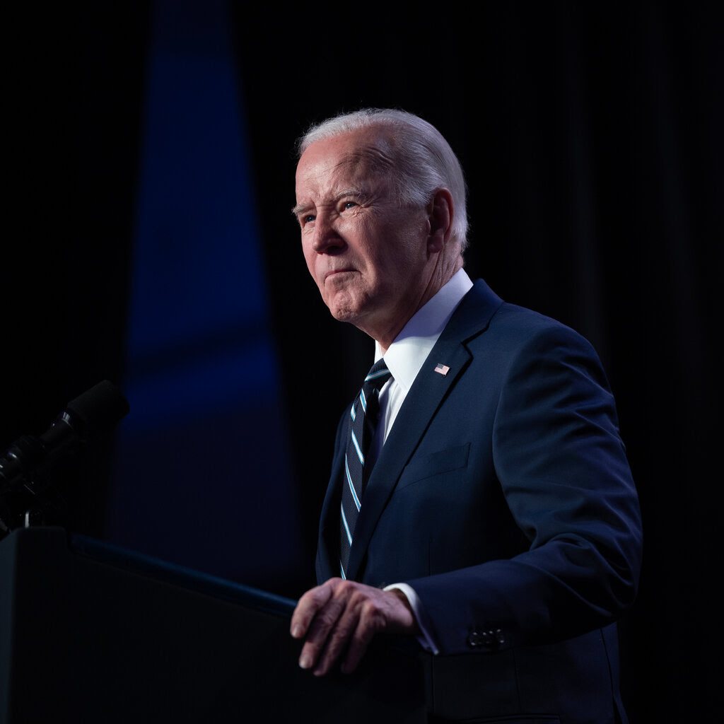 President Biden stands behind a podium wearing a blue suit.