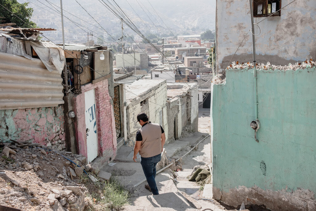 A rear view of a man in a cap walking down stone steps between shanty-like homes.