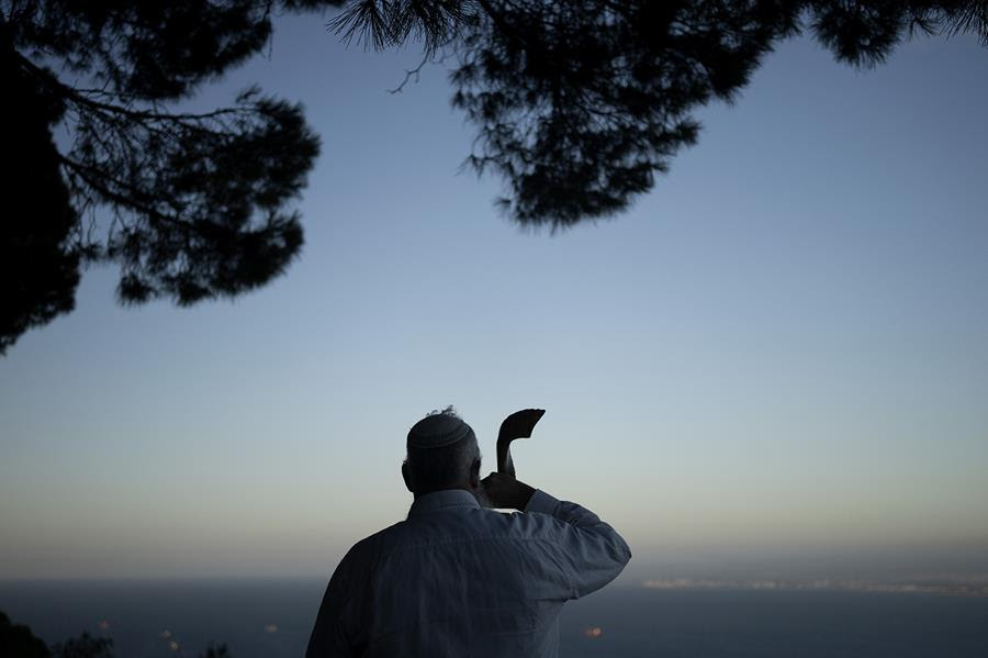 A man blowing a shofar (ram's horn) to mark the beginning of Rosh Hashana. He is standing with his back towards the viewer and the sun is setting.