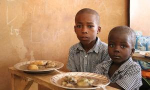 Dos niños estudiantes de primaria en Haití reciben el almuerzo gracias a un programa apoyado por la ONU.