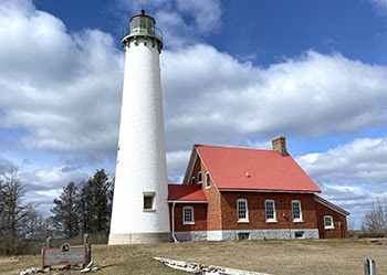 A tall, white lighthouse stands guard next to an attached brick-red building.