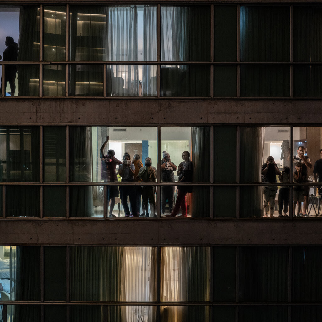 People standing on different floors inside a building and looking out the windows.