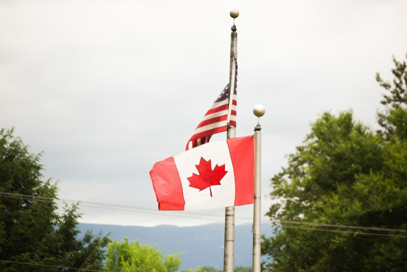 La bandera canadiense vuela junto a la bandera americana, con árboles y montañas en el fondo