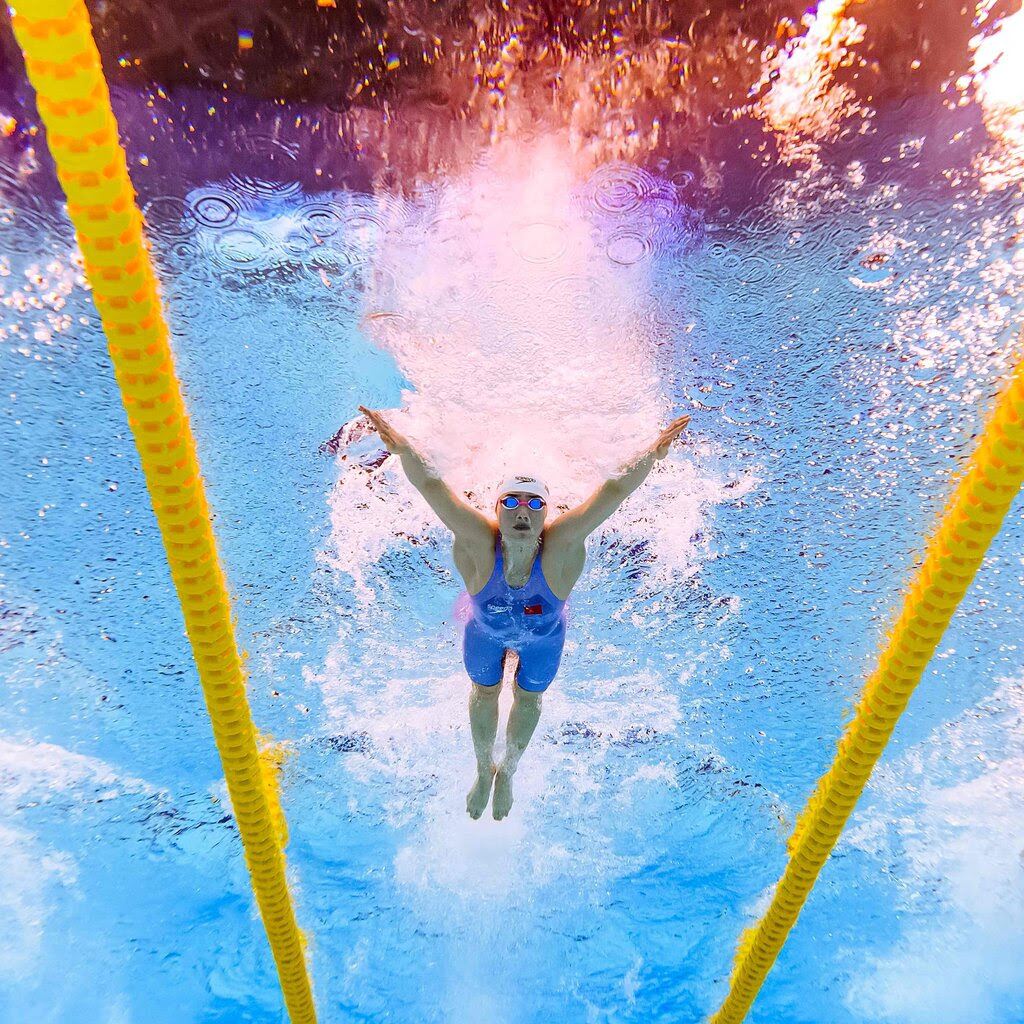 A picture of a swimmer in a pool, wearing a jumper-style swimsuit, from below