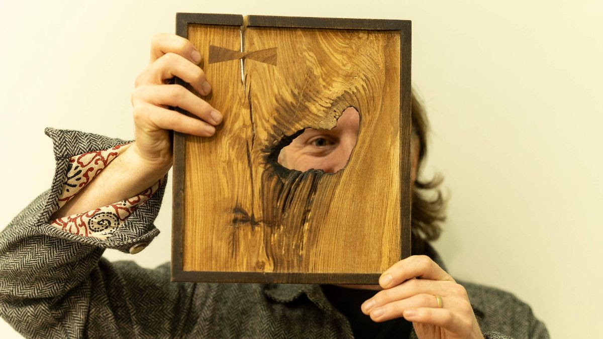 A person holding up a block of crafted wood looking through a hole in the wood.