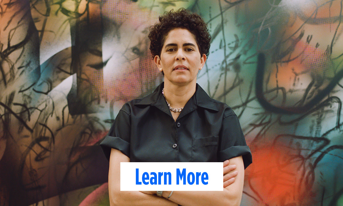 A woman with a short, curly afro and light to medium skin tone stands with her arms crossed in front of a colorful mural. A button at the bottom says "Learn More"