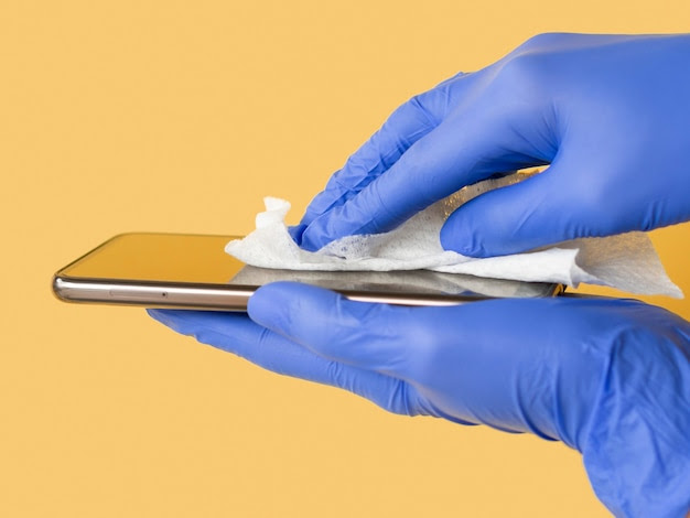 Side view of hands with surgical gloves disinfecting smartphone