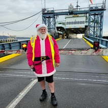 Person dressed as Santa Claus wearing a safety vest with a ferry docked in the background