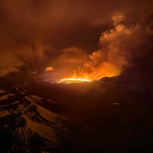 Smoke plumes rise from orange lava at night.