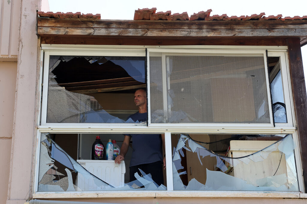 A man standing in a room and looking through a smashed window.