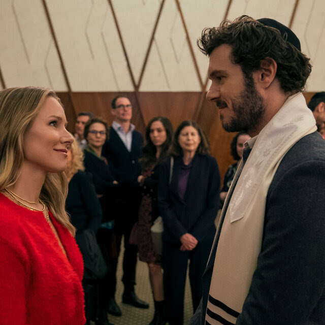 A woman in a red dress smiles up at a man in religious garments