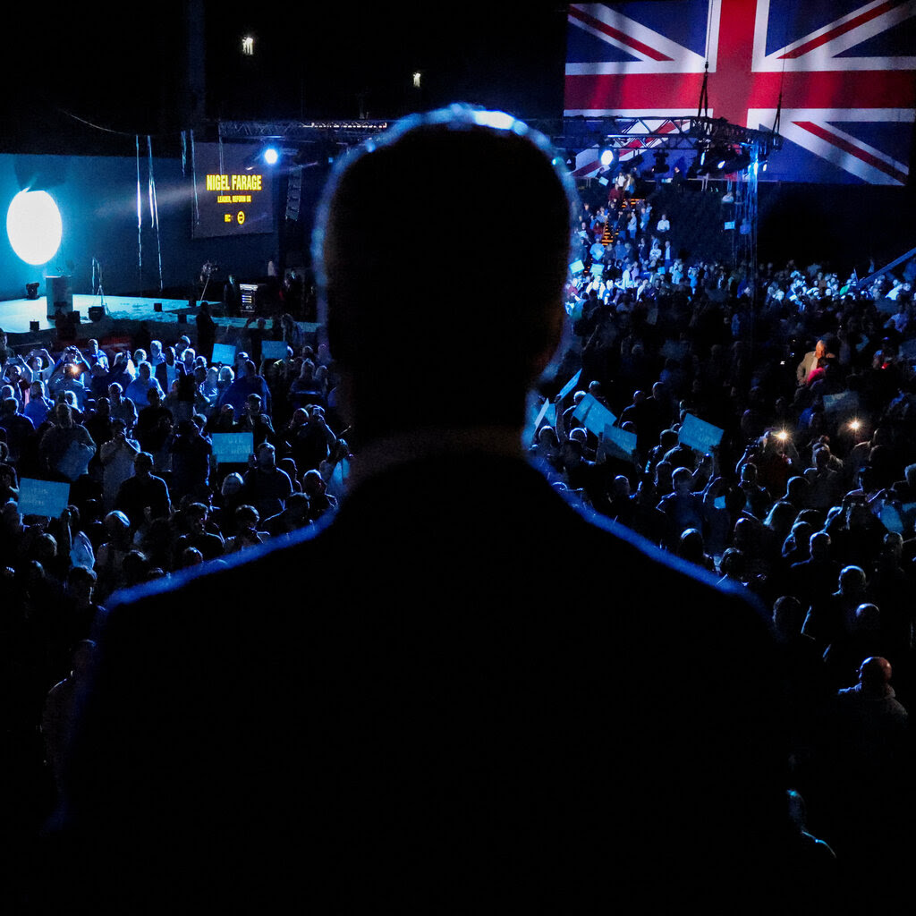The silhouette of the back of a man’s head, he’s standing at the back of a crowd. 