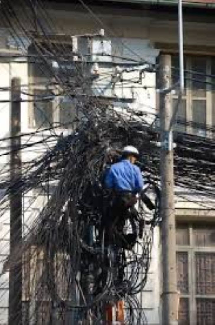Man up telephone pole amongst tons of wires.
