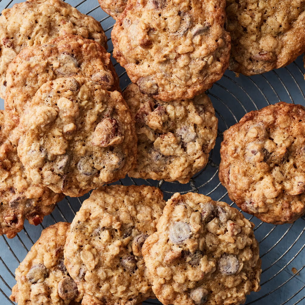 Oatmeal cookies with chocolate chips are piled on a wire baking rack.