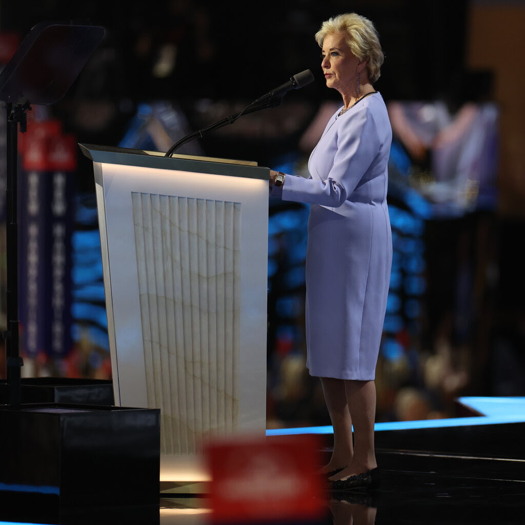 Linda McMahon, in a lavender dress, stands at a podium.