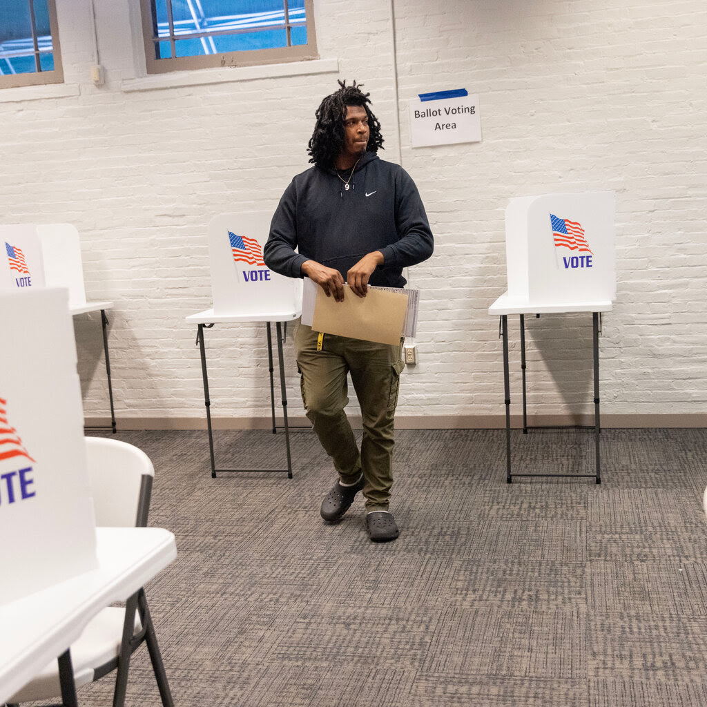 Ari Burroughs, who is wearing a black shirt and brown pants, walks away from a voting booth.